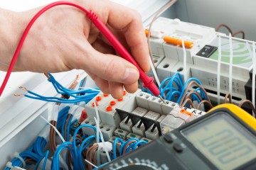 Hand of an electrician with multimeter probe at an electrical switchgear cabinet